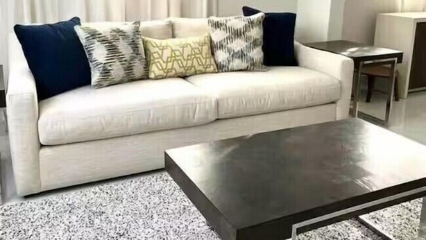 A living room with a white sofa, dark cushions, a coffee table, and a window with sheer curtains.
