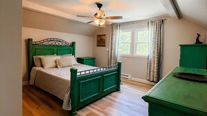 Ein Schlafzimmer mit einem grünen Bett, einem Deckenventilator, einem Fenster mit Vorhängen und einer grünen Kommode.