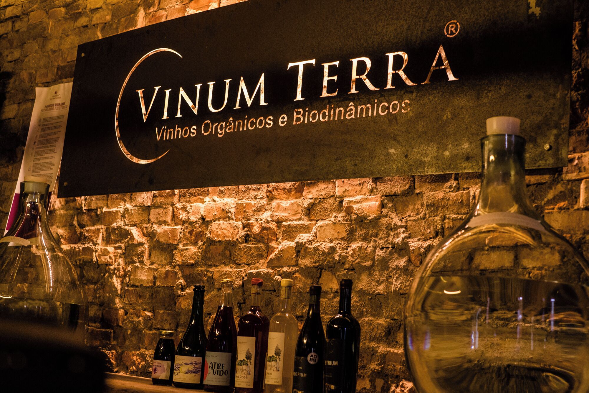 Uma adega com garrafas rotuladas "Vinum Terra" em frente a uma parede de tijolos.