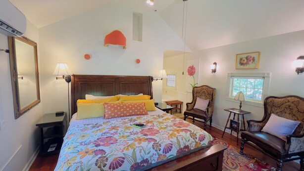 Ein Schlafzimmer mit einem großen Bett, zwei Stühlen, einem kleinen Tisch und einem Fenster.