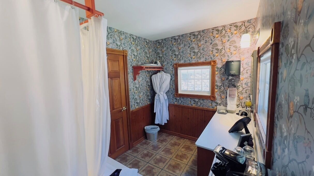 A bathroom with a shower curtain, a wooden door, a small window, a towel rack, a sink, and a mirror.