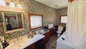 A bathroom with floral wallpaper, a sink with a mirror, a toilet, and a shower area.