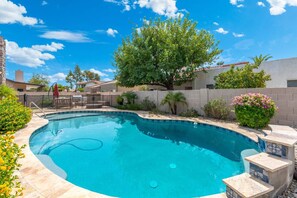A swimming pool with a stone border, surrounded by a fence, and various plants and trees. - Sun, Fun & a Tempe Tan Home (Tempe)