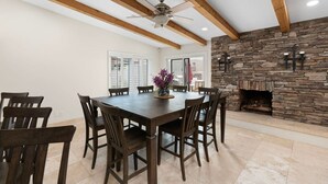 A dining area with a stone fireplace, wooden ceiling beams, and a ceiling fan. - Sun, Fun & a Tempe Tan Home (Tempe)