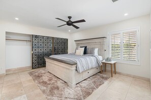 A bedroom with a bed, a ceiling fan, a window with blinds, a wardrobe, and a decorative screen. - Sun, Fun & a Tempe Tan Home (Tempe)