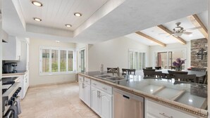A modern kitchen with a large island, white cabinetry, and a dining area with a stone accent wall. - Sun, Fun & a Tempe Tan Home (Tempe)