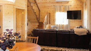 A cozy wooden cabin interior with a dining table, a sofa, a TV, and a staircase.