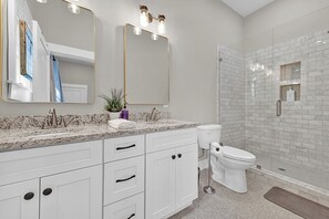 A modern bathroom with a marble countertop, white cabinets, a large mirror, and a glass-enclosed shower area. - Avondale Charmer-Comfort & Style (Birmingham)