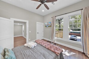 A bedroom with a bed, a ceiling fan, a window with curtains, and a door leading to another room. - Avondale Charmer-Comfort & Style (Birmingham)