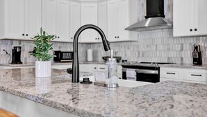 A kitchen with white cabinets, a granite countertop, a black faucet, and a stainless steel range hood. - Avondale Charmer-Comfort & Style (Birmingham)