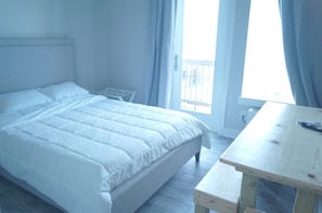Een slaapkamer met een bed, een houten nachtkastje, een raam met gordijnen en uitzicht op het omliggende landschap.