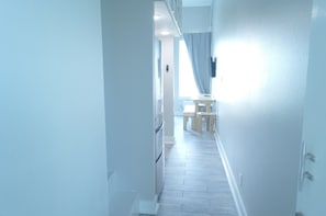 A narrow hallway with a wooden floor, a bench, and a table in the distance.