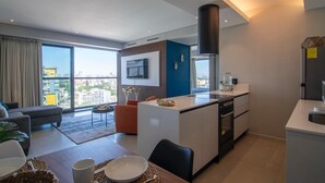 Un apartamento moderno con cocina, comedor y sala de estar. Cuenta con un amplio ventanal, televisor de pantalla plana y vista a la ciudad.