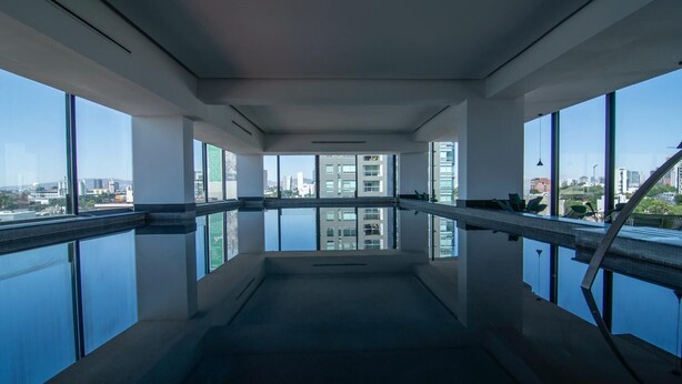 Una piscina interior moderna con paredes de vidrio transparente que ofrece vistas al paisaje urbano.