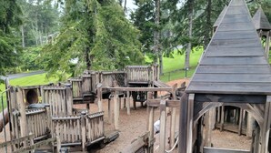 A wooden play structure with multiple levels and slides, surrounded by trees. - Coastal Adventures, Lake, Ocean, Casinos, Hiking (Neotsu)
