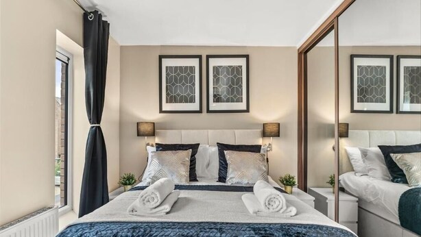 Habitación de hotel con cama, dos mesitas de noche, ventana con cortinas y cuadros en la pared.