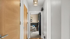 Un pasillo con piso de madera, una puerta blanca y un candelabro colgante.