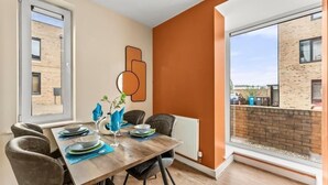 Comedor con una mesa de madera dispuesta para cuatro personas, un radiador y vista a un edificio de ladrillo a través de una ventana.