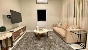 Un salon avec un canapé beige, une table basse, un téléviseur et un appareil de climatisation.