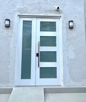 Una puerta doble blanca con paneles de vidrio esmerilado y un pomo negro, flanqueada por dos apliques de pared.