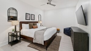 Ein modernes Schlafzimmer mit Bett, Nachttischen, Deckenventilator, Fernseher und Kommode.