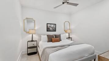 A bedroom with a bed, bedside tables, lamps, a ceiling fan, and a framed picture on the wall.