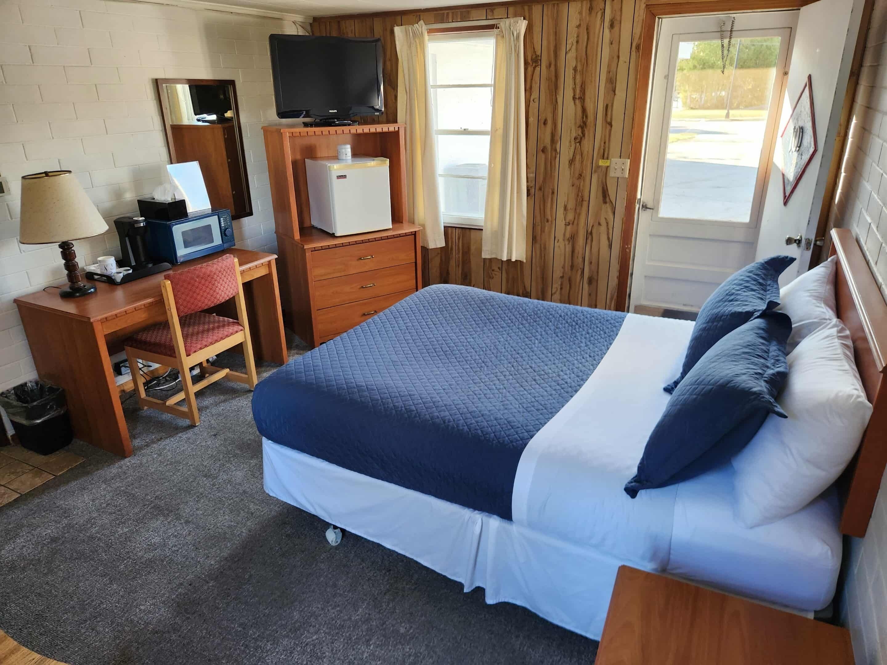 A hotel room with a bed, a desk with a computer, a TV, and a small refrigerator.