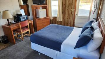 A hotel room with a bed, a desk with a computer, a TV, and a small refrigerator.