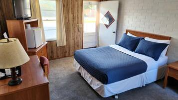 Une chambre d’hôtel avec un lit, un bureau avec une lampe, une télévision et une porte avec une fenêtre.