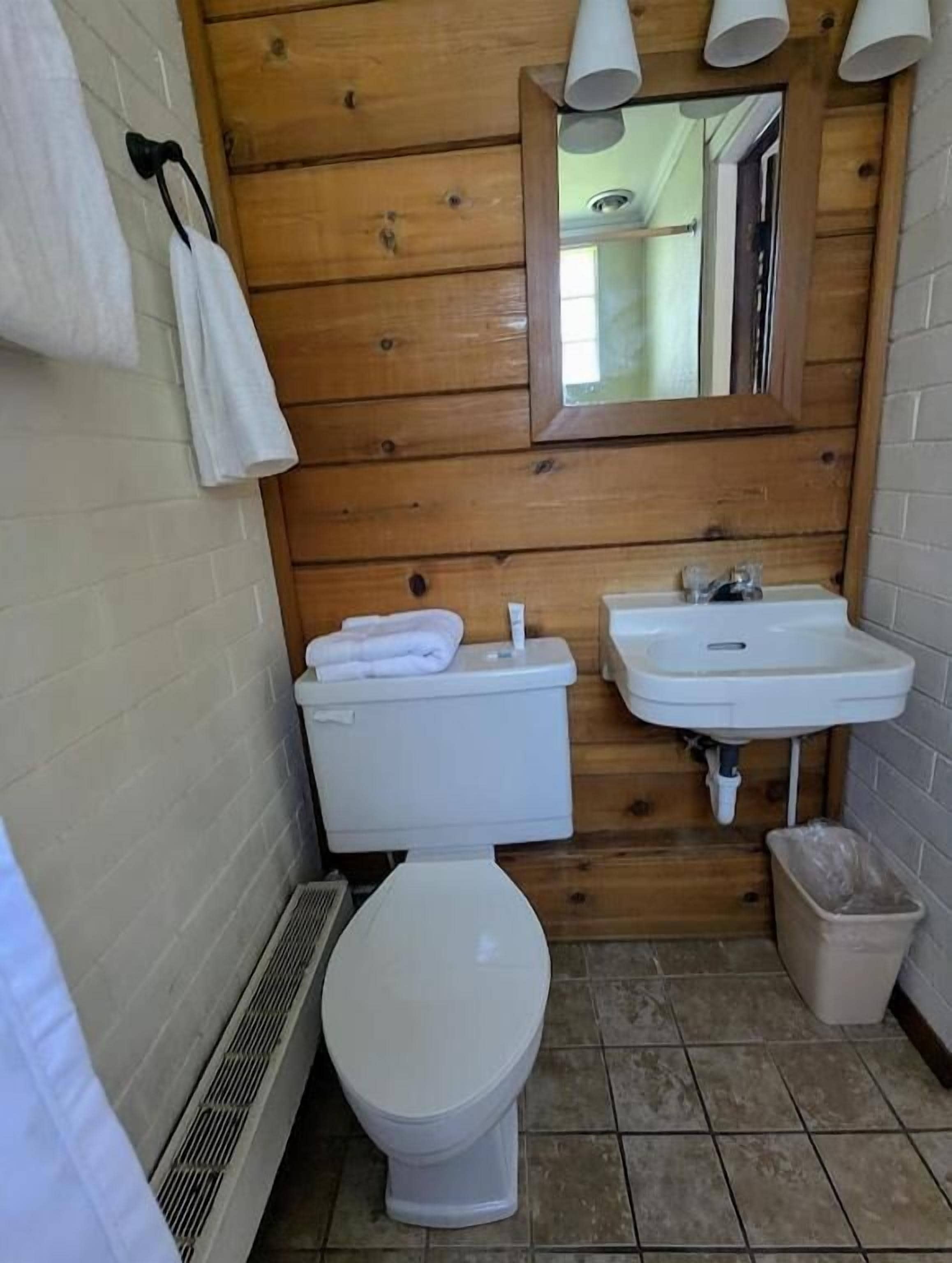 Ein kleines, kompaktes Badezimmer mit Holzvertäfelung, einer weißen Toilette, einem Waschbecken und einem Spiegel.