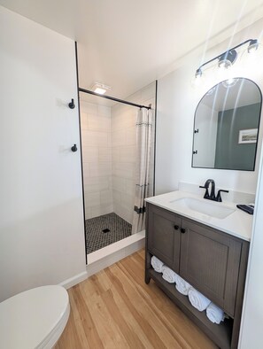 A modern bathroom with a shower, toilet, sink, and a mirror with lights.