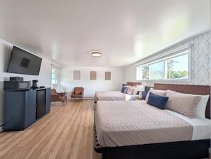 A hotel room with two beds, a TV, a desk with a computer, and a window with a view.