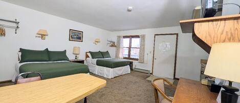 Ein Zimmer mit zwei Betten, einem Schreibtisch, einem Sessel, einem Fernseher und einem Fenster.