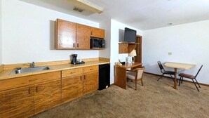 A compact kitchen with wooden cabinets, a microwave, a sink, and a small dining area with a table and chairs. - Cool City Motel  (Two Rivers)