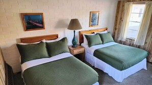 A hotel room with two beds, each with green bedding and white sheets. There are two paintings on the walls, a lamp on the nightstand, and a window with curtains. - Cool City Motel  (Two Rivers)
