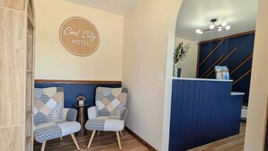 A reception area with a sign reading 'Cool City Motel,' two patterned chairs, a wooden reception desk, and a ceiling light fixture. - Cool City Motel  (Two Rivers)