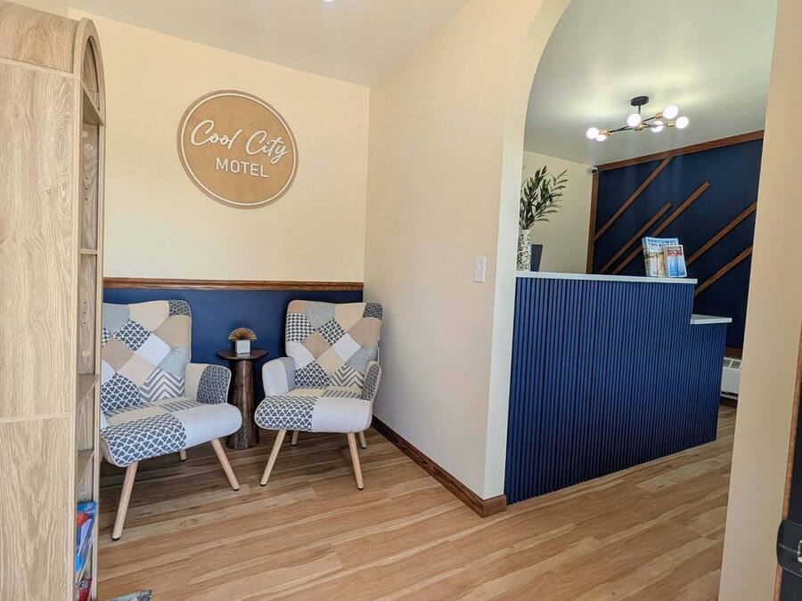 Een receptie met een bord waarop 'Cool City Motel' staat, twee gestreepte stoelen, een houten receptiebalie en een plafondlamp.