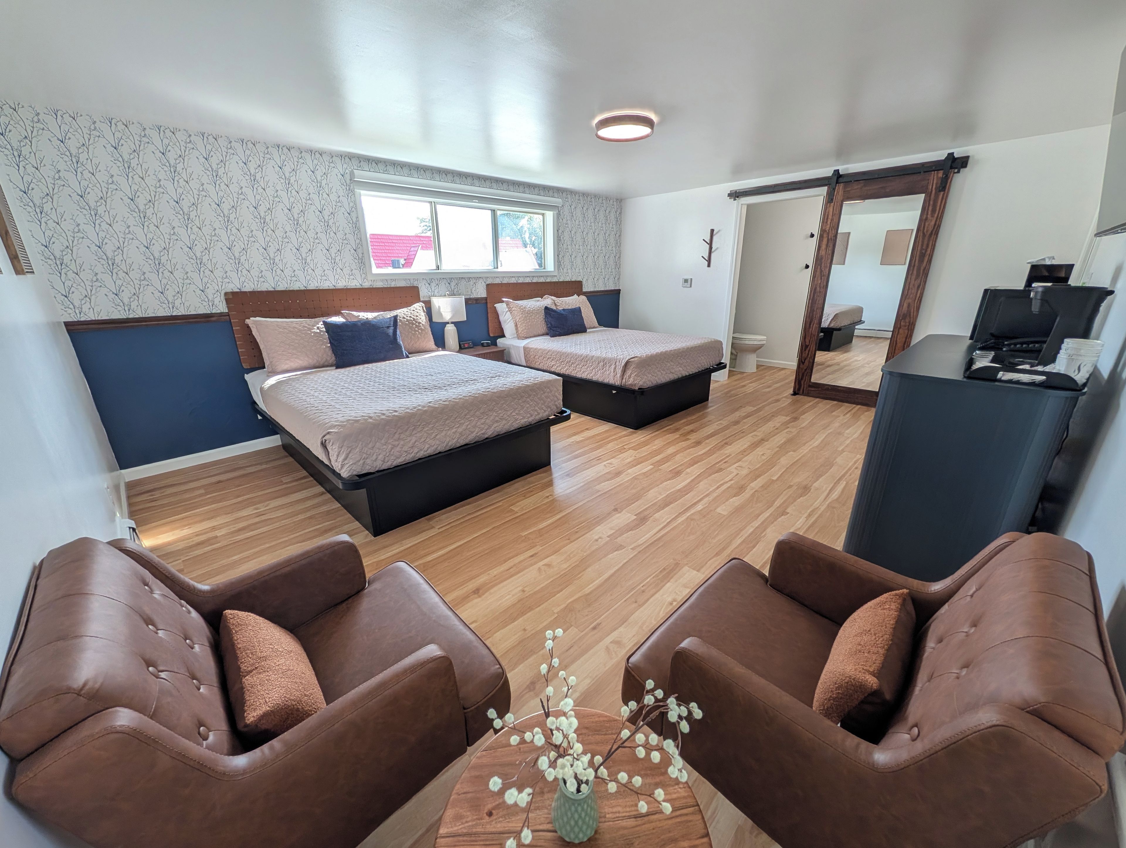 Ein Hotelzimmer mit zwei Betten, einer Sitzecke mit Sesseln, einem kleinen Tisch und einem Fenster.
