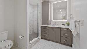 Un baño moderno con cabina de ducha de vidrio, inodoro, lavamanos con espejo y tocador con cajones.