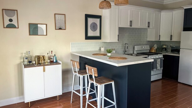 Una cocina moderna con gabinetes blancos, una isla central con taburetes, una estufa y un refrigerador.