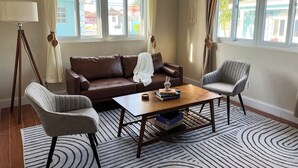 Una sala de estar con un sofá de cuero marrón, dos sillones grises, una mesa de centro de madera y una alfombra estampada.