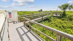 A wooden boardwalk leading through a lush green landscape with a small pavilion in the distance. - Ocean Gate I104 (St. Augustine)