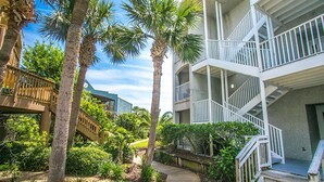 A multi-story hotel with a wooden deck, palm trees, and a staircase leading to the upper floors. - Ocean Gate I104 (St. Augustine)