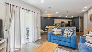 A modern living room with a blue sofa, wooden coffee table, and a view of the kitchen in the background. - Ocean Gate I104 (St. Augustine)