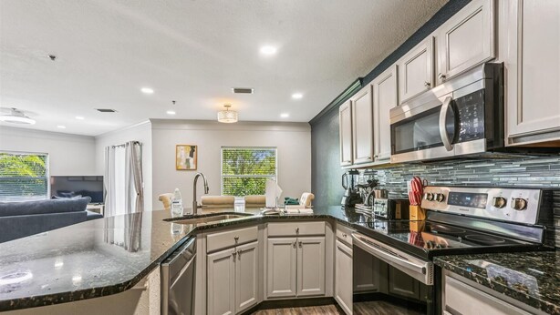 A modern kitchen with white cabinetry, a large island, stainless steel appliances, and a view of the outdoors. - Ocean Gate I104 (St. Augustine)
