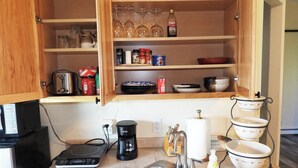 Una cucina con lavello in acciaio inox, una macchina da caffè, un tostapane e diversi utensili ed elettrodomestici da cucina.
