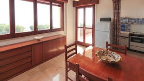 A kitchen with wooden cabinets, a dining table, and a view through large windows. - Bongiovi Houses - App. Azure - 2 min from the beach, with garden and sea view (Sicilia)