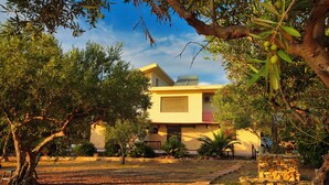 A modern house with a yellow facade, surrounded by trees and a stone pathway. - Bongiovi Houses - App. Azure - 2 min from the beach, with garden and sea view (Sicilia)