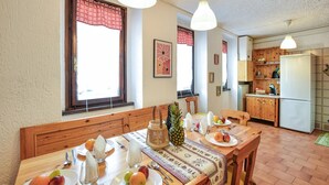 A dining area with a wooden table set for two, a pineapple, and fruit on plates. There are two pendant lights above the table, and a kitchen area with wooden cabinets and a refrigerator in the background. - 2 bedroom lovely apartment in Ponte di Legno (Ponte di Legno)