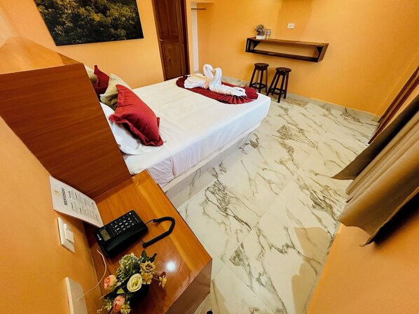 Una camera d'albergo con un letto, una scrivania con il telefono e un tavolino con un vaso di fiori.